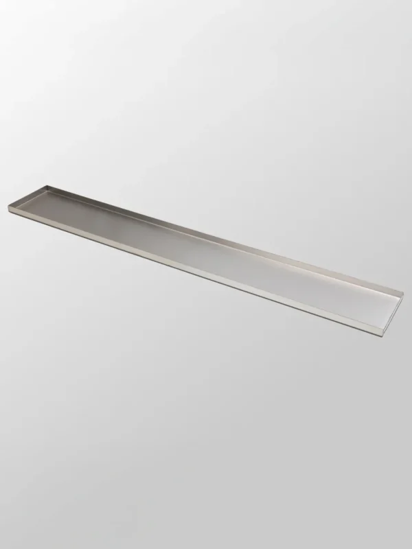 Dekorbricka Lång, en långsmal rektangulär bricka i borstat rostfritt stål med upphöjda kanter, mot en enfärgad ljusgrå bakgrund.