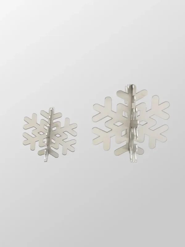 Två snöflingor i 3D-metall från Snöflinga 2-pack, tillverkade i borstat rostfritt stål, ligger sida vid sida på en ljusgrå bakgrund. Den vänstra snöflingan är mindre än den högra.